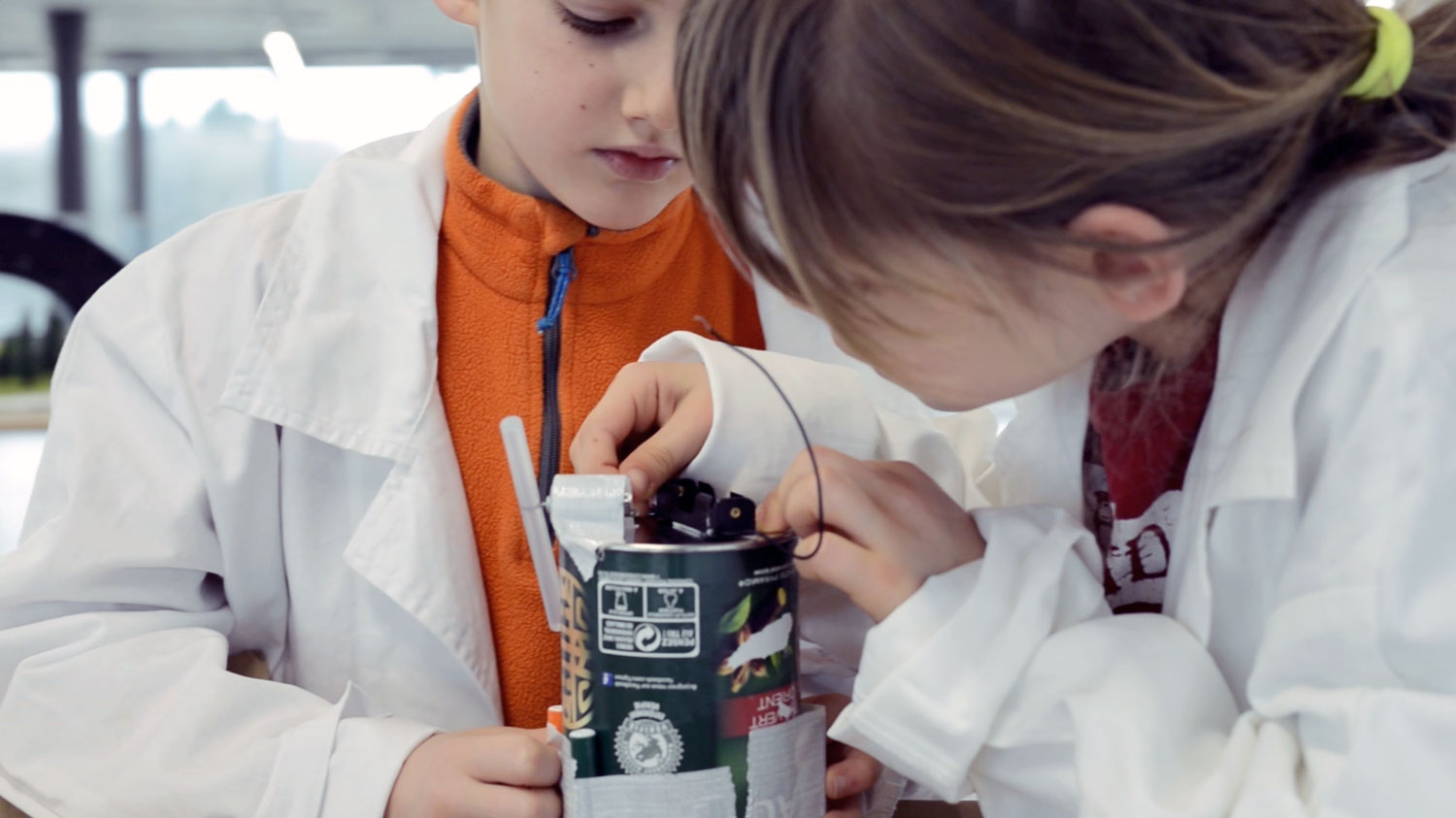 Two kids in a laboratory building a scribbling robot with an empty can.