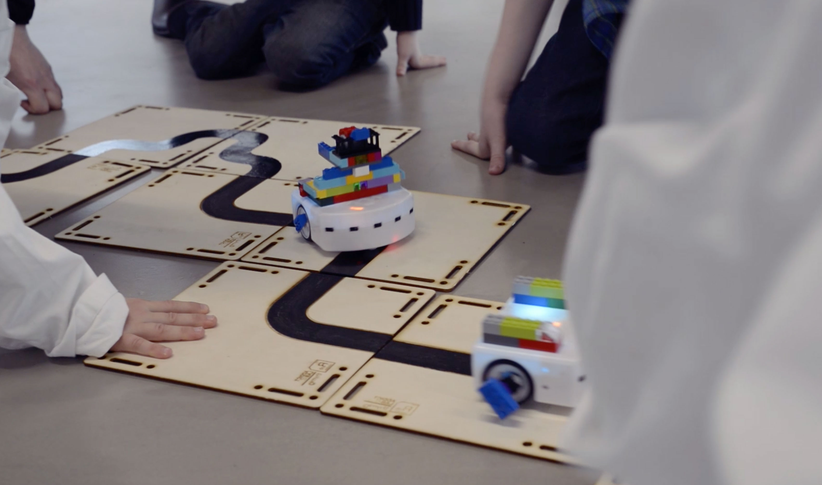 Kids playing with Epfl's Thymio robots on laser cut wooden tracks made by Addictlab Academy during a birthday party